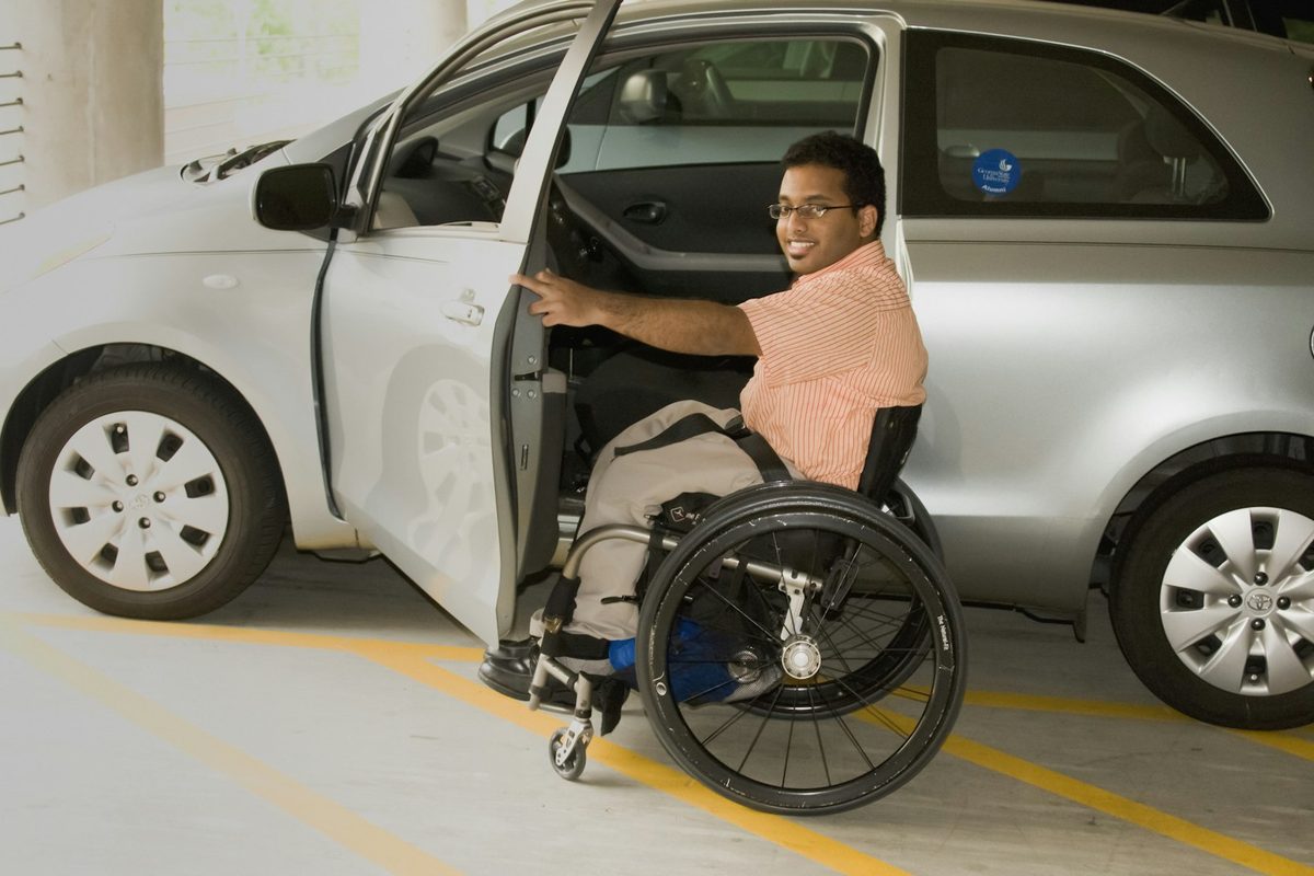 Un homme en fauteuil roulant, souriant, ouvre la portière d’une voiture grise