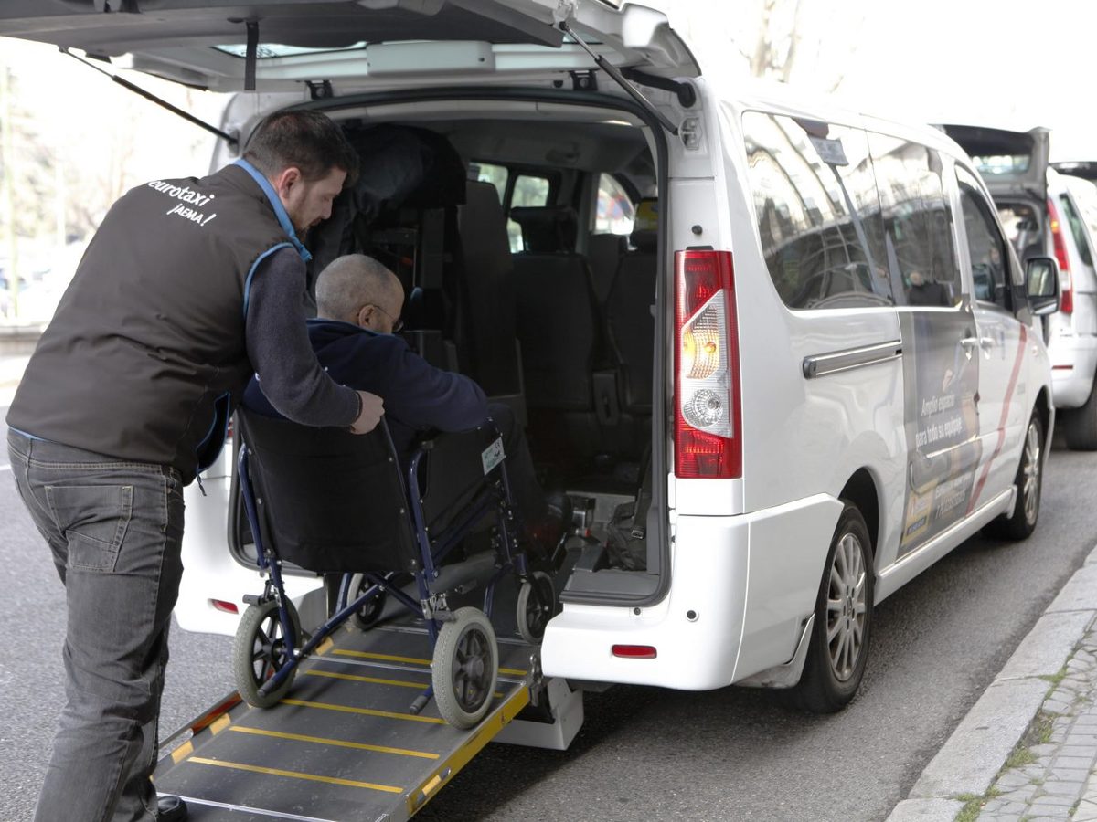 Une personne en fauteuil roulant monte par la rampe arrière d’un véhicule adapté, aidée par un accompagnant